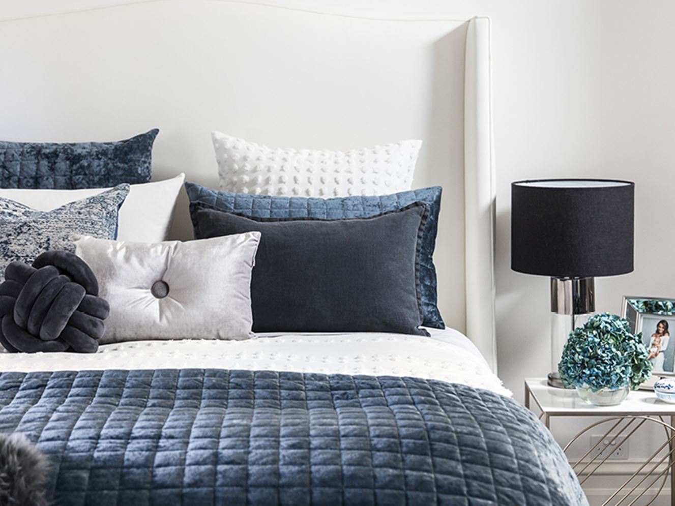 Luxurious navy blue coverlet and matching pillowcases, styled against a white textured quilt cover and decorative cushions in velvet silver and vintage blue.